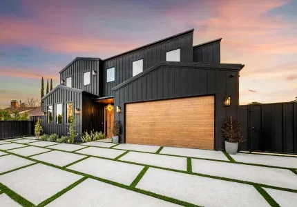 Modern black-sided home with wood garage door at dusk